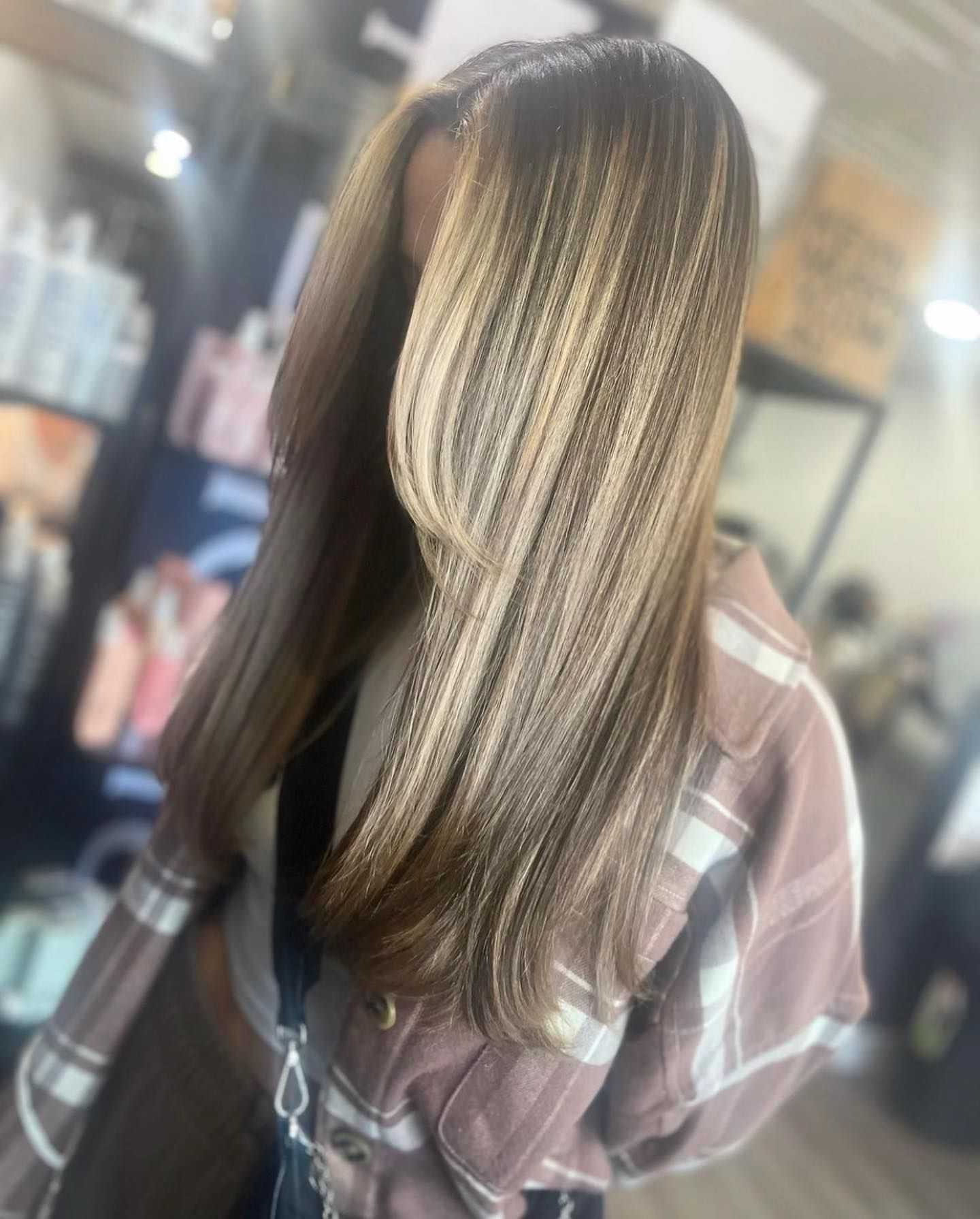 Woman with long, highlighted hair wearing a plaid shirt in a salon.