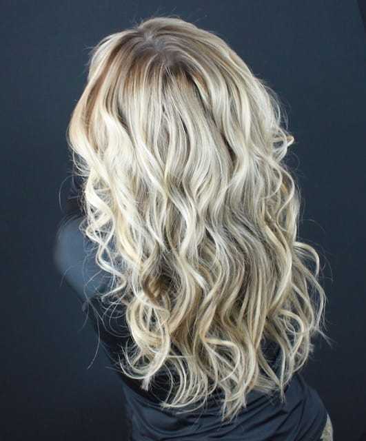 Person with long, wavy, blonde hair seen from behind against a dark background.