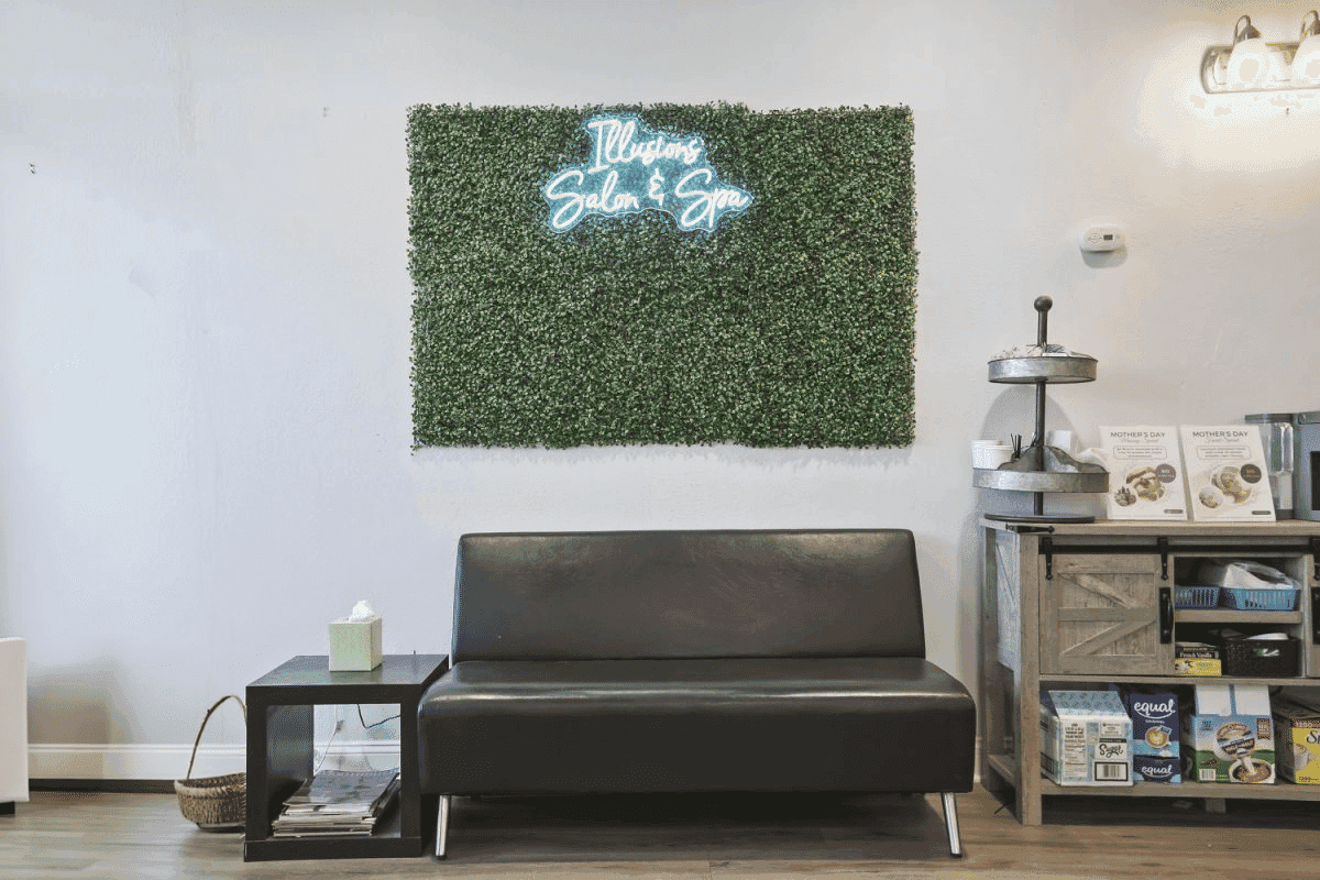 Black couch and side table in a salon lobby, with a neon "Welcome Salon & Spa" sign on a green wall.
