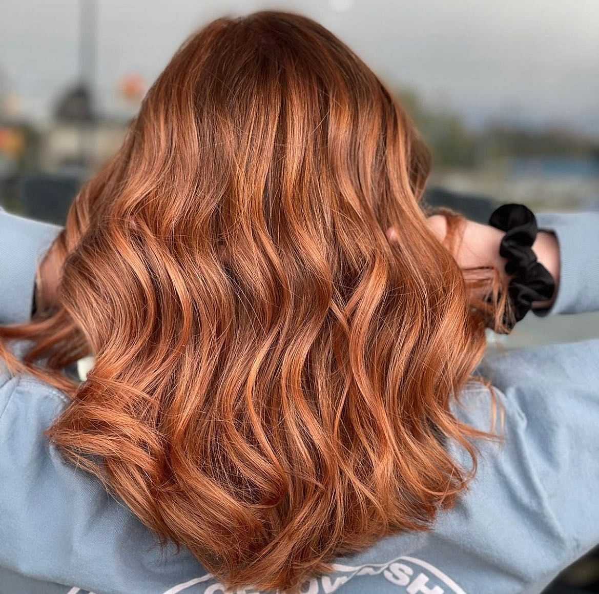 Wavy auburn hair styled in loose curls, seen from the back, with a person wearing a light blue sweater.