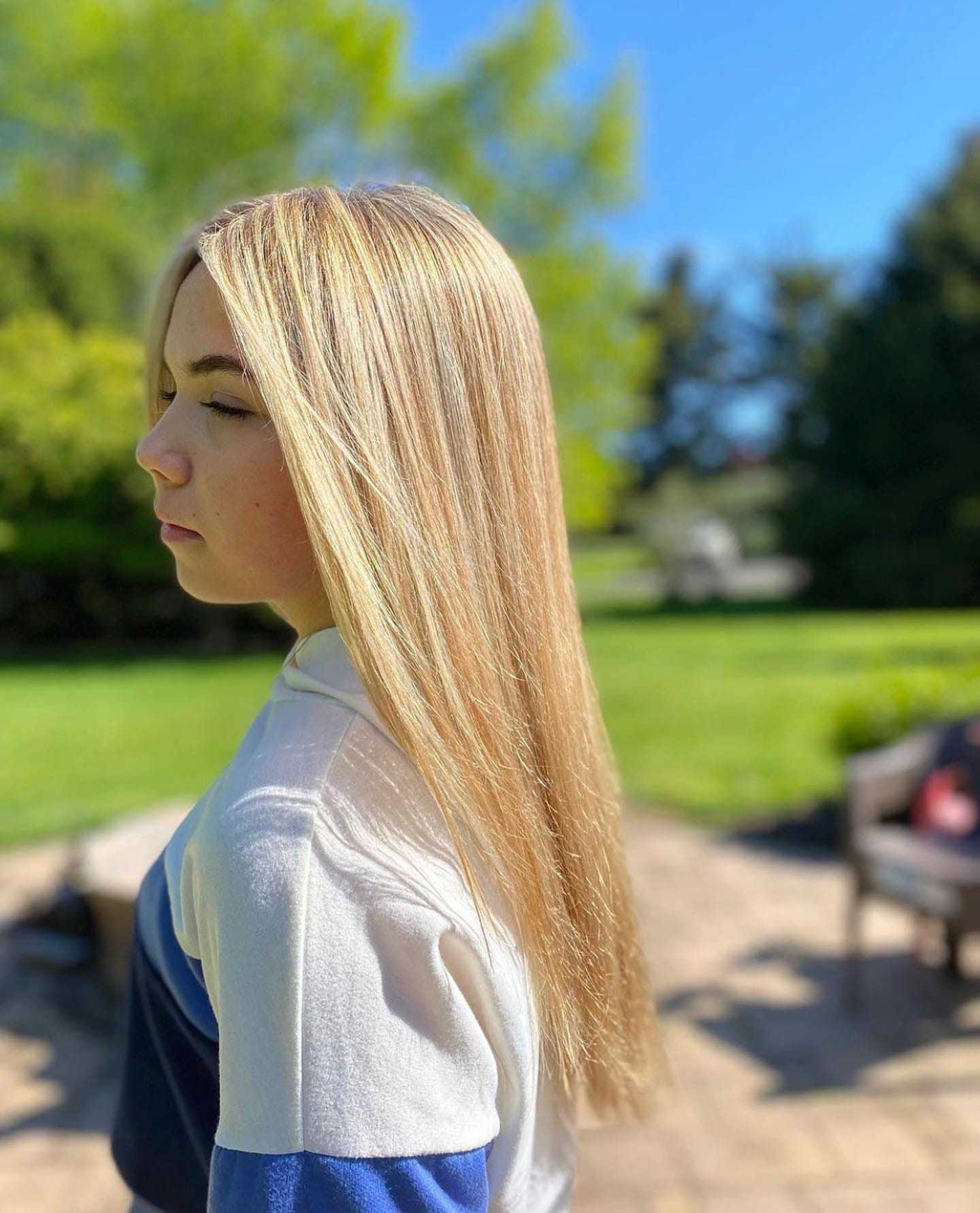 Woman with straight blonde hair outside on a sunny day, wearing a white and blue top.