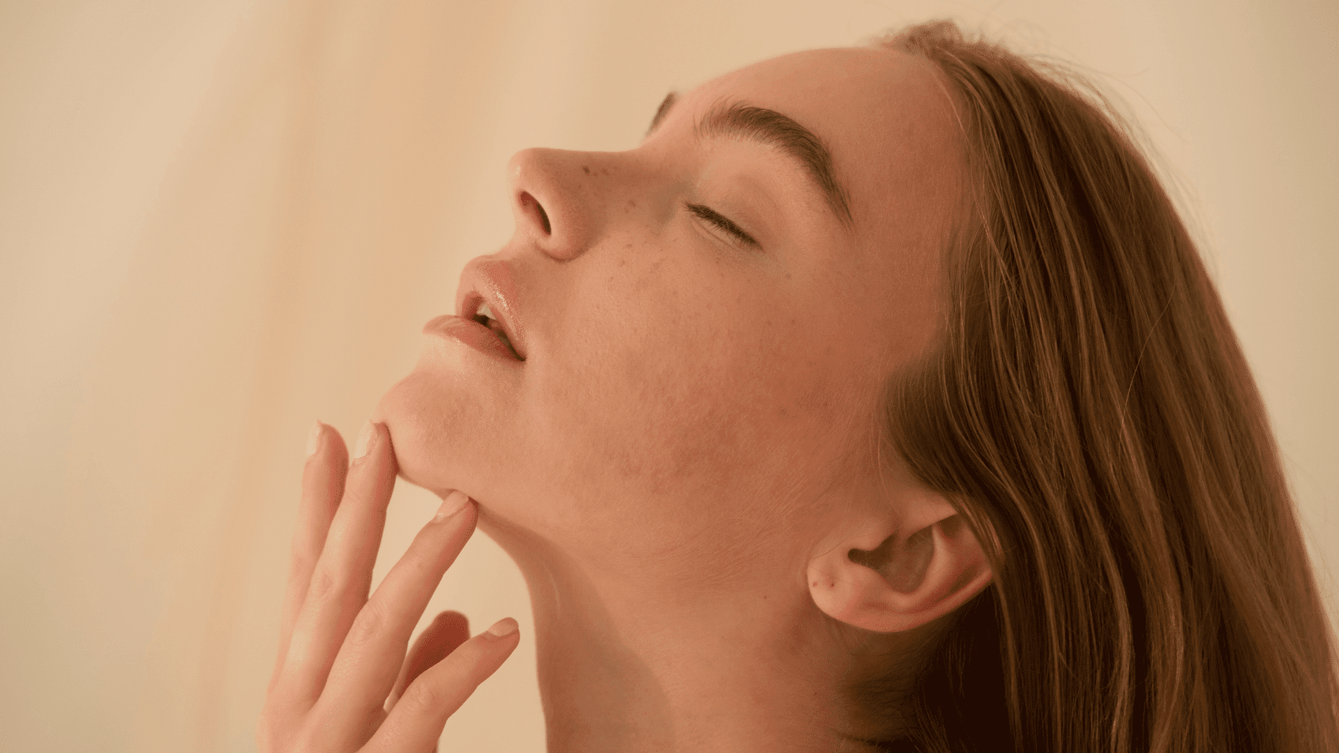 Young woman with closed eyes and serene expression, fingers gently touching her chin.