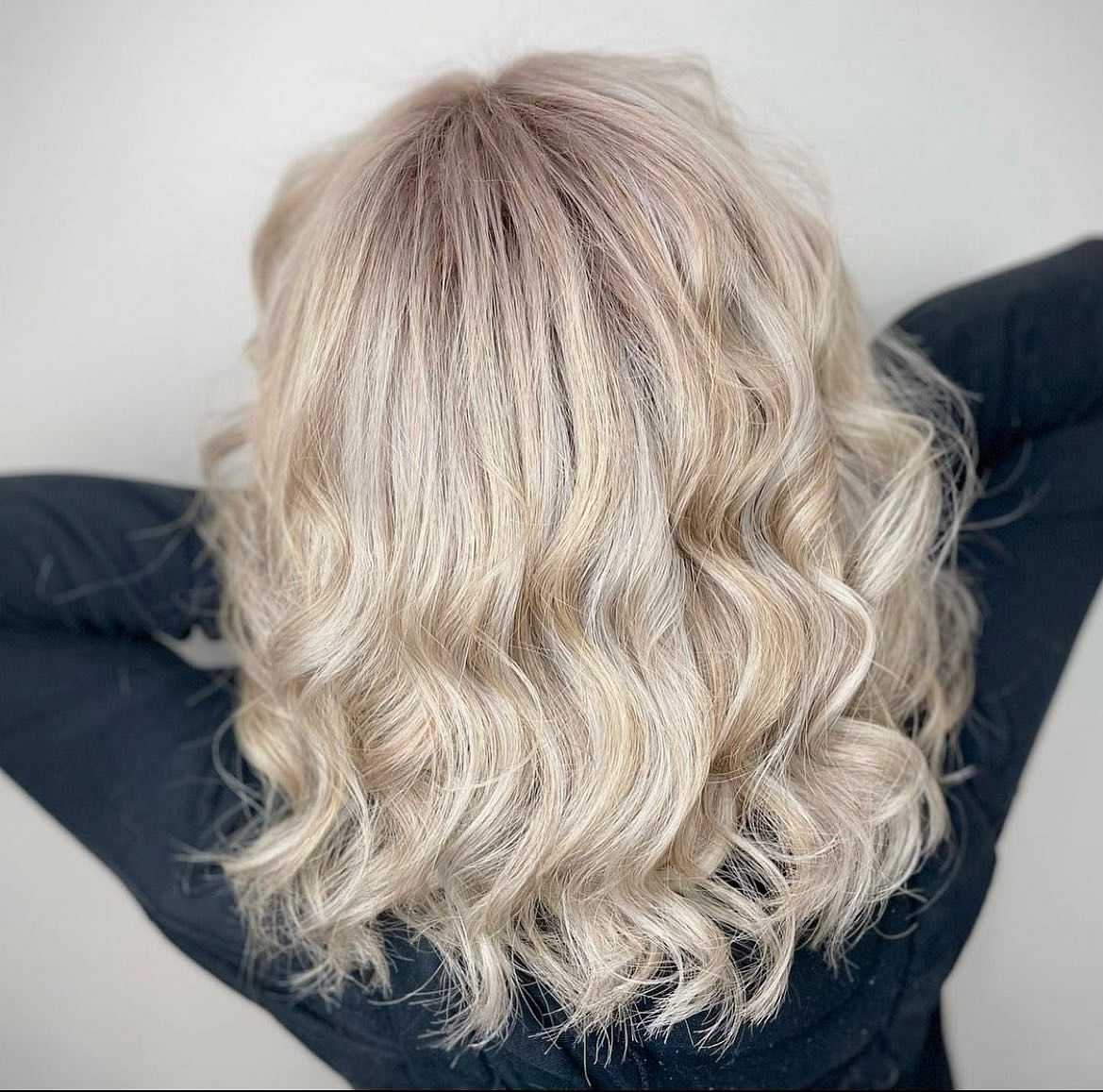 Wavy blonde hair styled in loose curls, viewed from the back against a plain background.