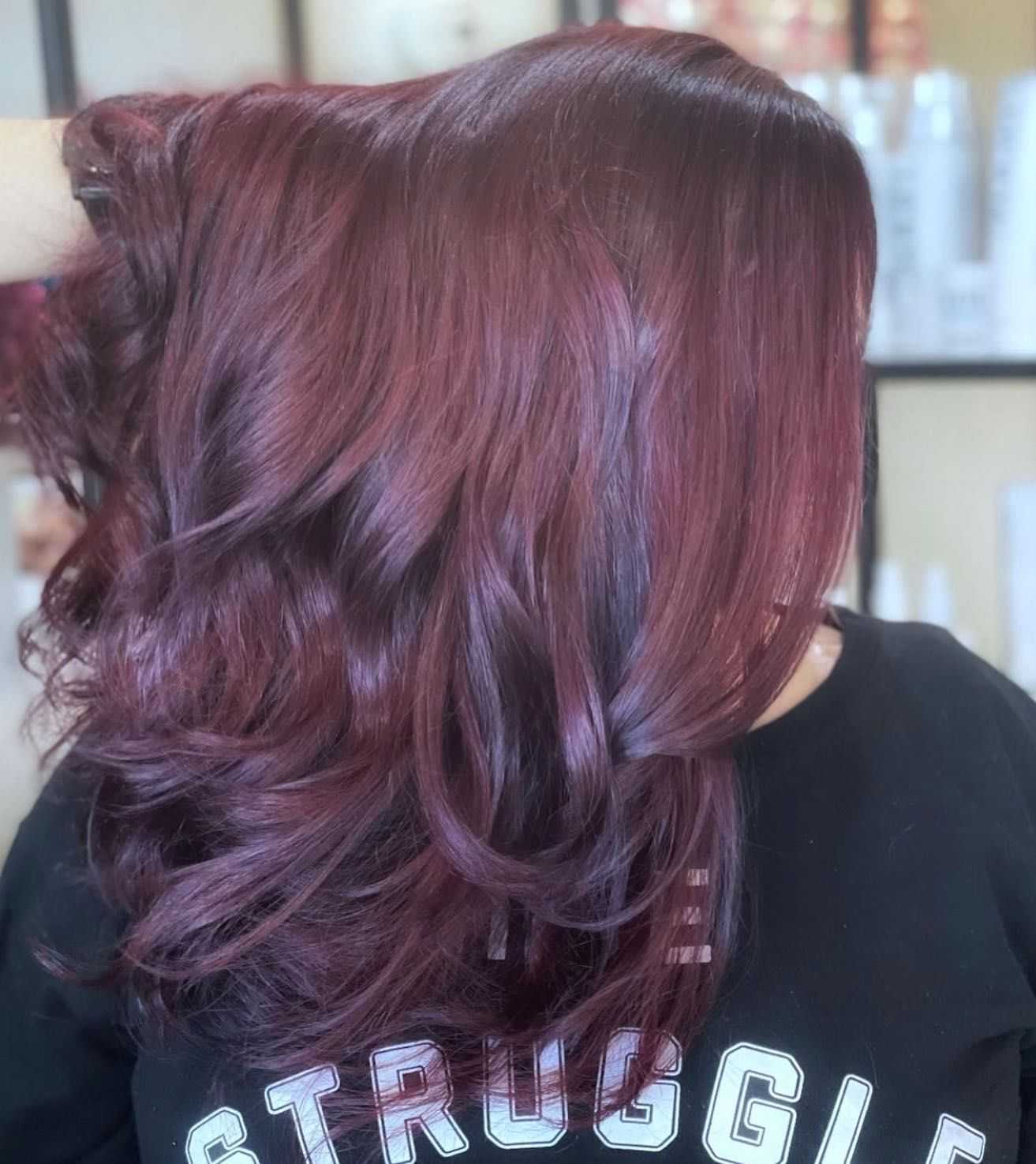 Person with wavy, shoulder-length maroon hair, wearing a black shirt with "STRUGGLE" written across.
