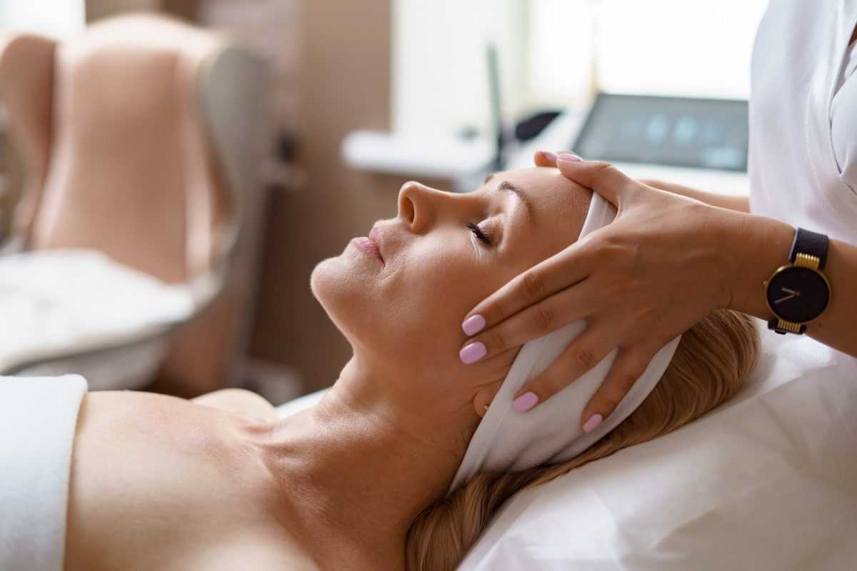 Woman receiving a relaxing facial massage at a spa, lying down with eyes closed.