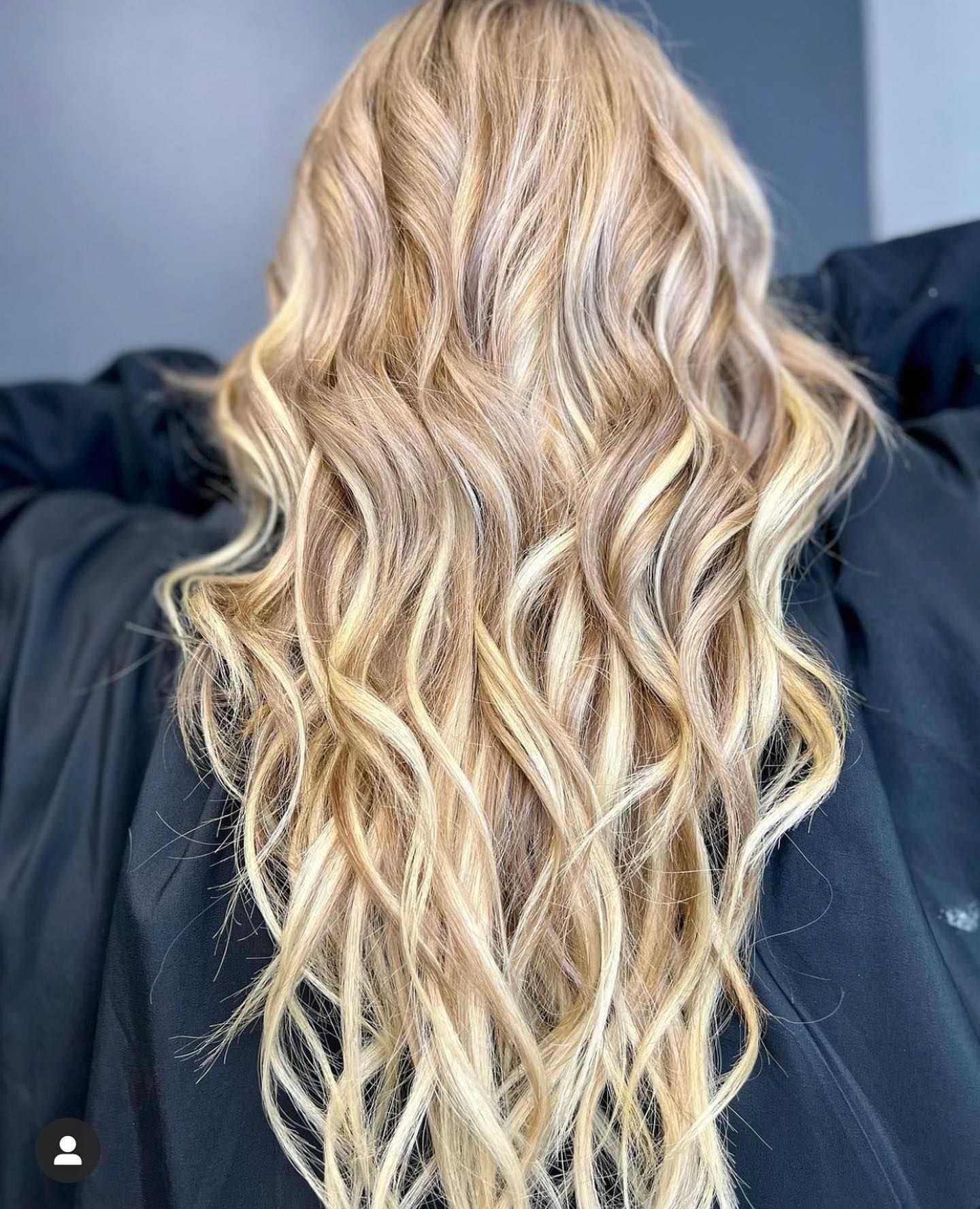 Blonde wavy hair styled in loose curls, viewed from the back against a dark background.
