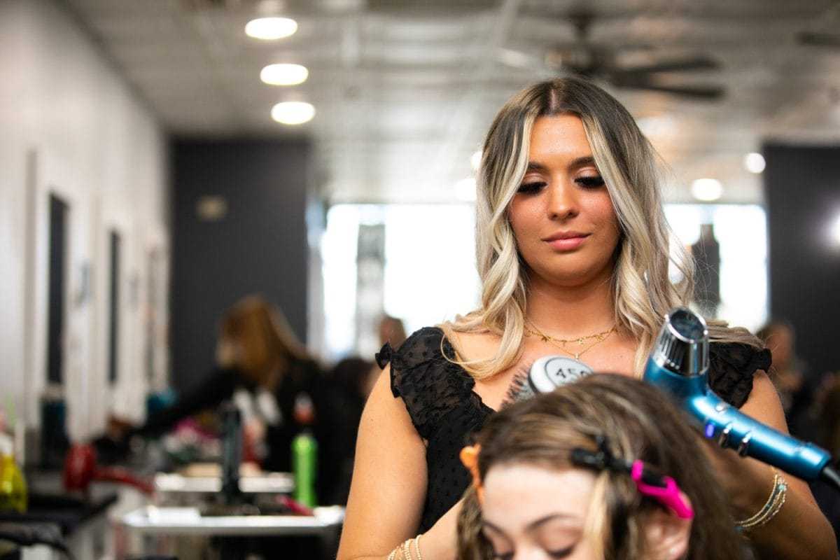 Woman styling a young girl's hair in a busy salon.